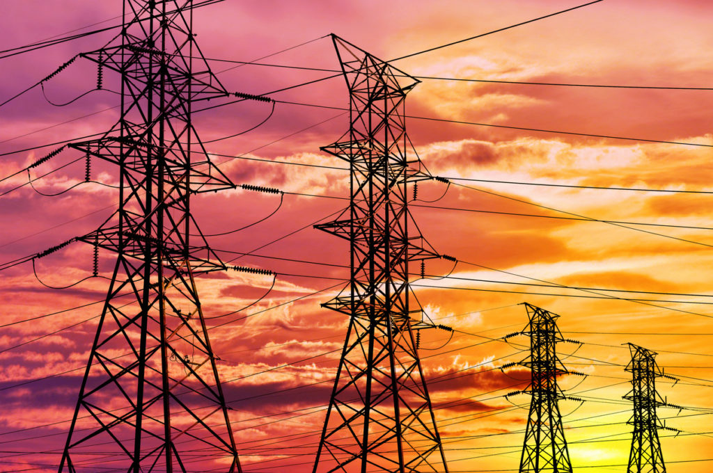 Row of electrical towers with high voltage cables set against a vibrant sunset.